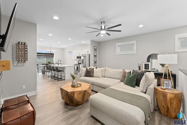 living room featuring ceiling fan with notable chandelier and light hardwood / wood-style flooring