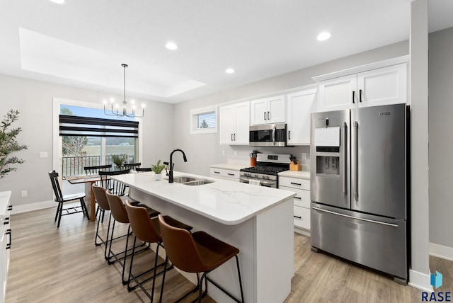 kitchen with sink, stainless steel appliances, a tray ceiling, an island with sink, and white cabinets