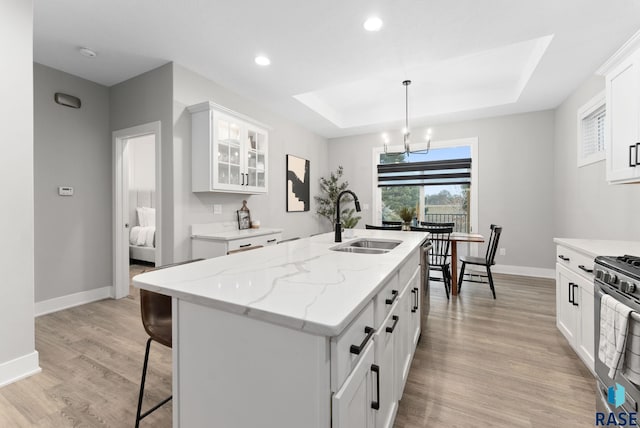 kitchen with pendant lighting, sink, an island with sink, white cabinets, and a raised ceiling