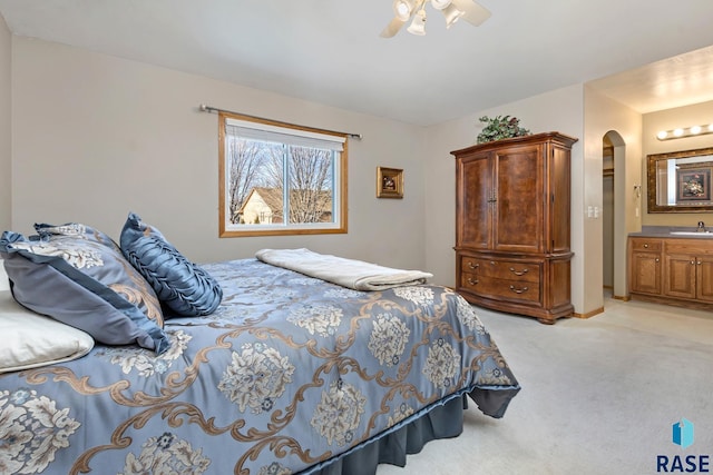 bedroom featuring connected bathroom, light colored carpet, sink, and ceiling fan