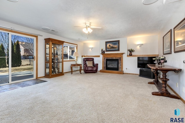 living area featuring ceiling fan, carpet floors, a tile fireplace, and a textured ceiling