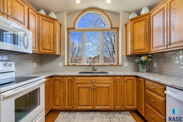 kitchen featuring light stone counters, sink, white appliances, and backsplash