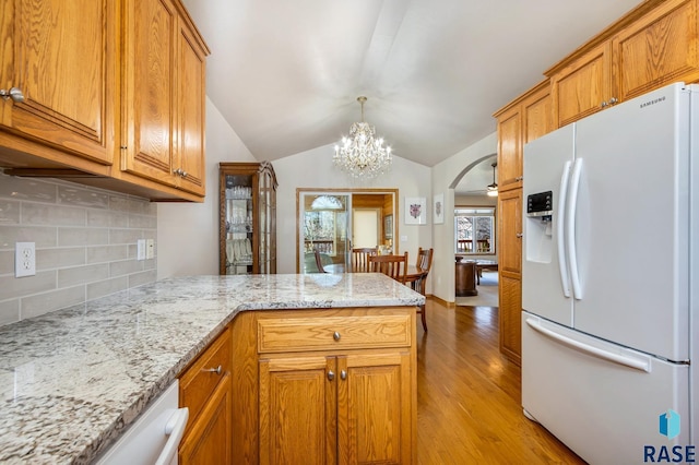 kitchen with lofted ceiling, white fridge with ice dispenser, light stone countertops, light hardwood / wood-style floors, and backsplash