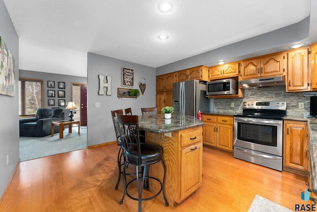 kitchen with tasteful backsplash, appliances with stainless steel finishes, a center island, and a kitchen bar