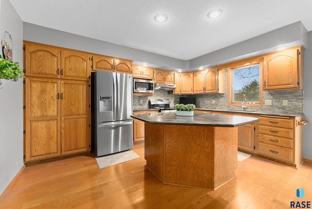 kitchen featuring sink, backsplash, stainless steel appliances, a center island, and light wood-type flooring