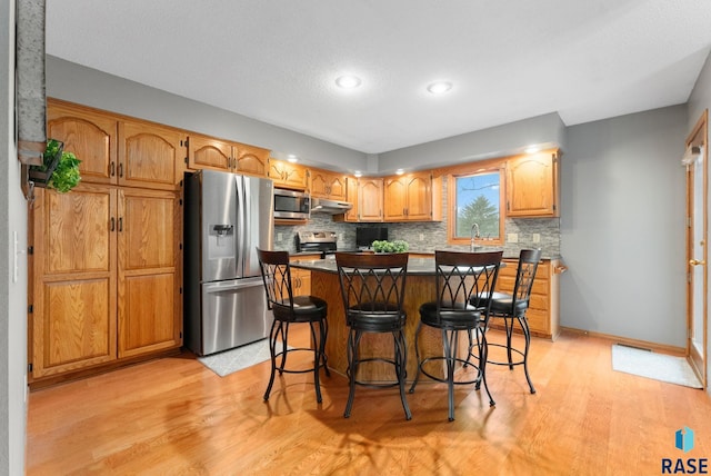 kitchen featuring appliances with stainless steel finishes, a breakfast bar area, decorative backsplash, a center island, and light hardwood / wood-style floors