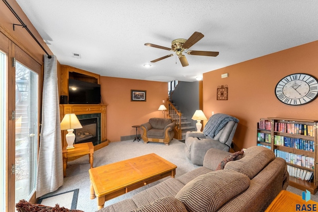 carpeted living room featuring ceiling fan, a fireplace, and a textured ceiling