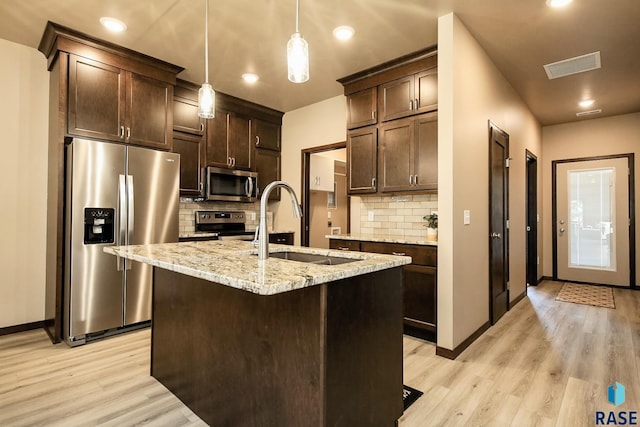 kitchen featuring a kitchen island with sink, light stone countertops, decorative light fixtures, and stainless steel appliances