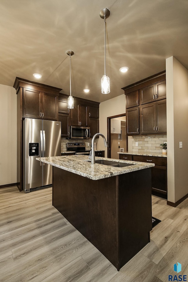 kitchen with stainless steel appliances, decorative light fixtures, an island with sink, and dark brown cabinets