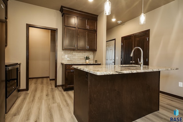 kitchen with pendant lighting, backsplash, an island with sink, and electric range