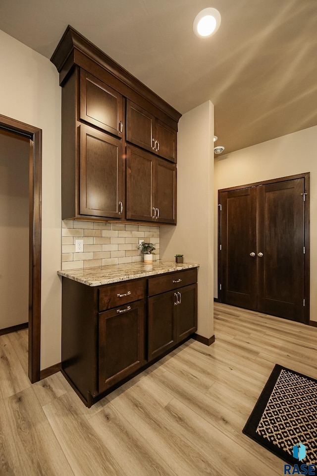 kitchen featuring light stone countertops, decorative backsplash, dark brown cabinets, and light hardwood / wood-style floors