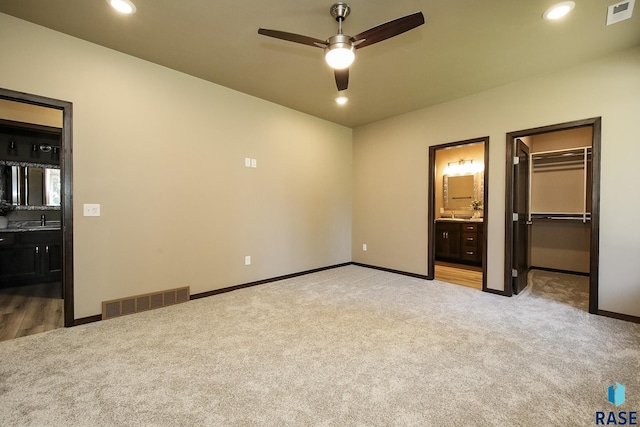 unfurnished bedroom with sink, ensuite bathroom, light carpet, a spacious closet, and a closet