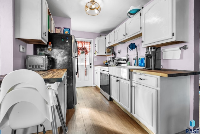 kitchen featuring white cabinetry, butcher block countertops, stainless steel range, and light hardwood / wood-style floors