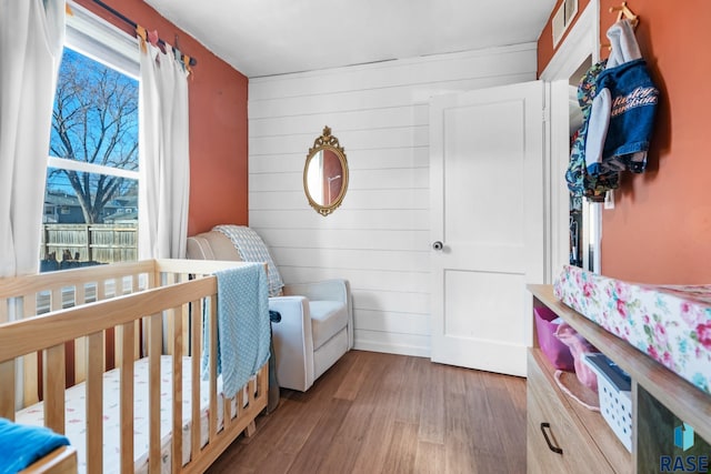 bedroom featuring hardwood / wood-style floors, wooden walls, and a nursery area