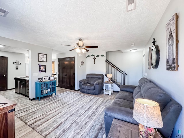 living room featuring ceiling fan, a textured ceiling, and light wood-type flooring