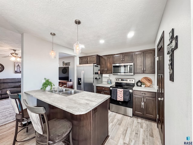 kitchen with pendant lighting, sink, appliances with stainless steel finishes, light hardwood / wood-style floors, and kitchen peninsula