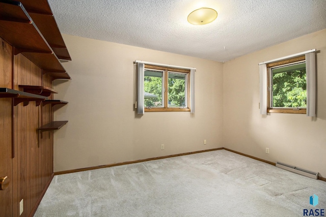 carpeted spare room featuring a baseboard radiator, plenty of natural light, and a textured ceiling