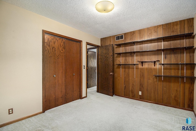 unfurnished bedroom featuring light colored carpet, wood walls, a textured ceiling, and a closet