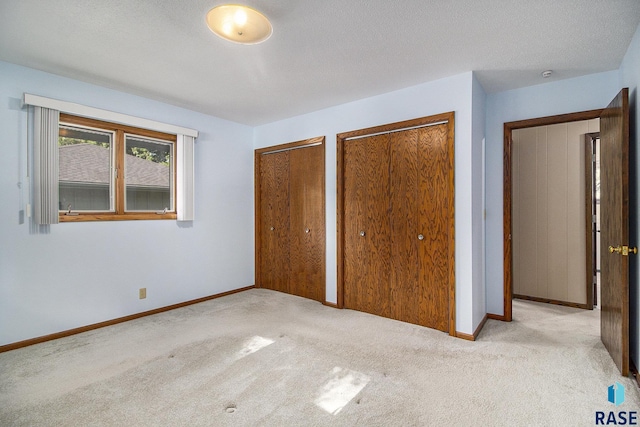 unfurnished bedroom with multiple closets, light carpet, and a textured ceiling