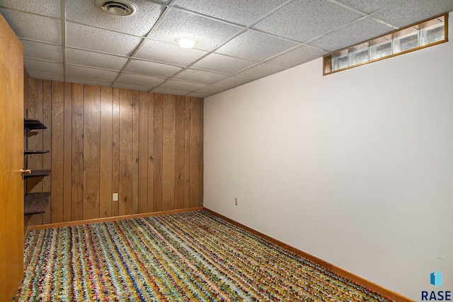 basement featuring a drop ceiling, carpet floors, and wood walls