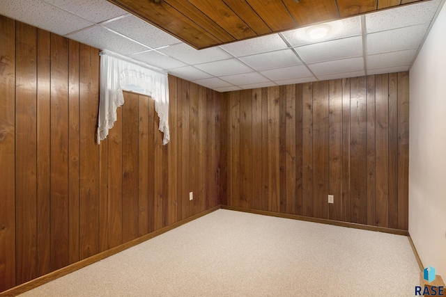 basement featuring a drop ceiling, carpet floors, and wood walls