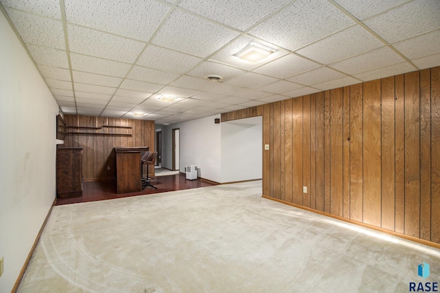 basement with carpet flooring, wooden walls, and a paneled ceiling