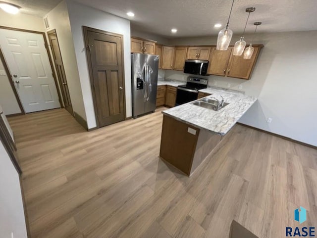 kitchen featuring sink, appliances with stainless steel finishes, hanging light fixtures, light hardwood / wood-style floors, and kitchen peninsula