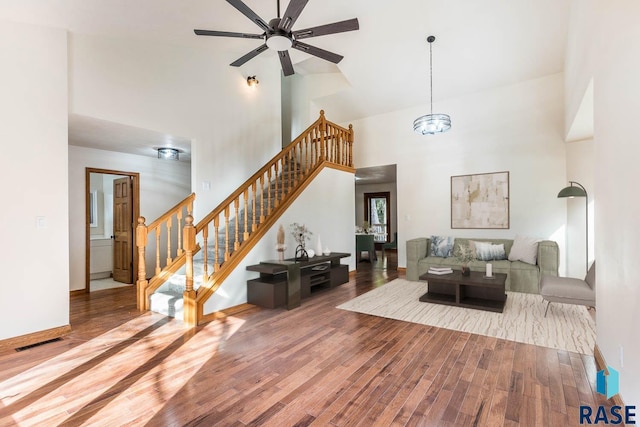 living room with hardwood / wood-style flooring, ceiling fan with notable chandelier, and a high ceiling