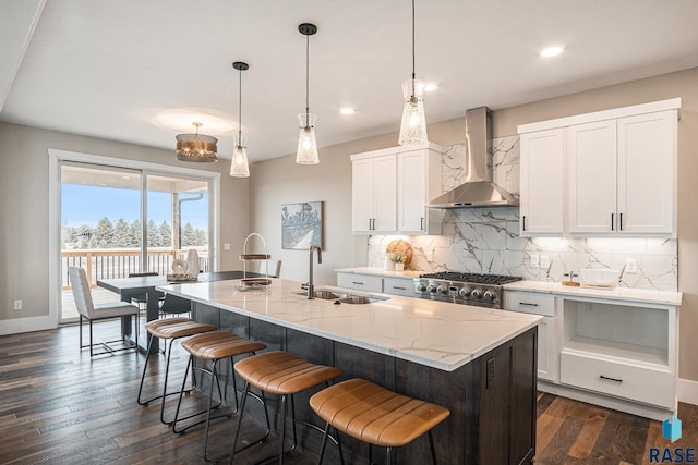 kitchen with white cabinetry, wall chimney range hood, sink, and a center island with sink