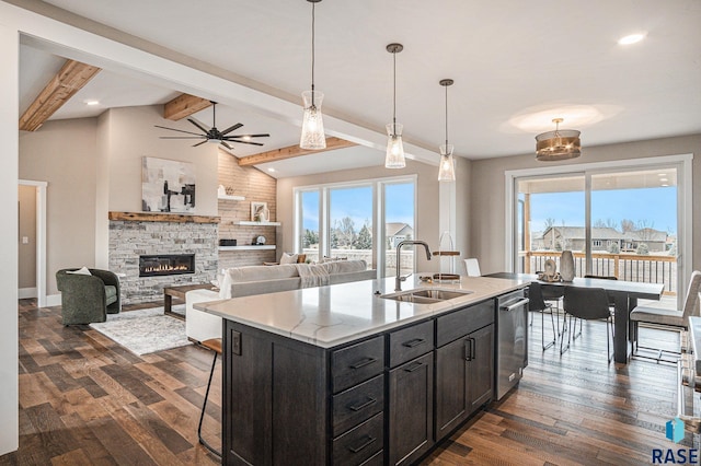 kitchen featuring a fireplace, decorative light fixtures, an island with sink, sink, and vaulted ceiling with beams