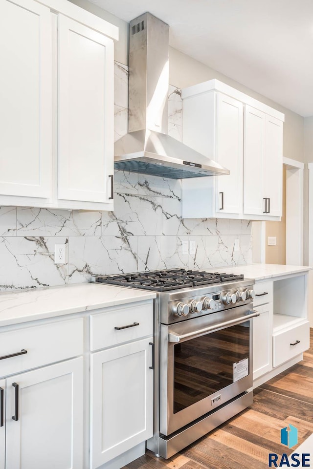 kitchen featuring white cabinets, stainless steel range, light stone countertops, and wall chimney range hood