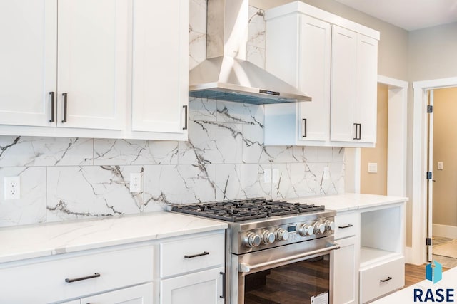 kitchen with wall chimney range hood, high end range, backsplash, light stone counters, and white cabinets