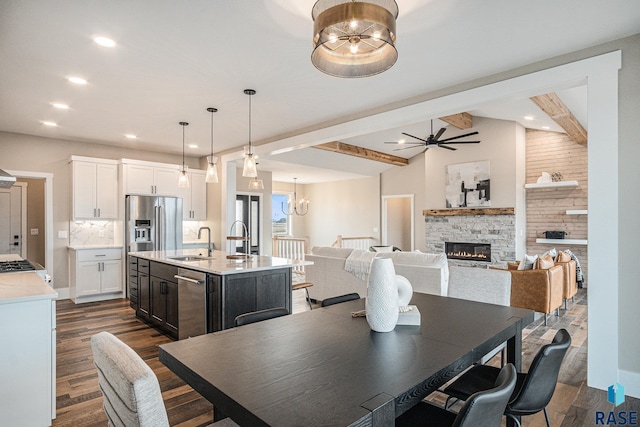 dining area featuring dark hardwood / wood-style floors, ceiling fan with notable chandelier, a fireplace, lofted ceiling with beams, and sink