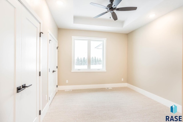 spare room with light carpet, a raised ceiling, and ceiling fan