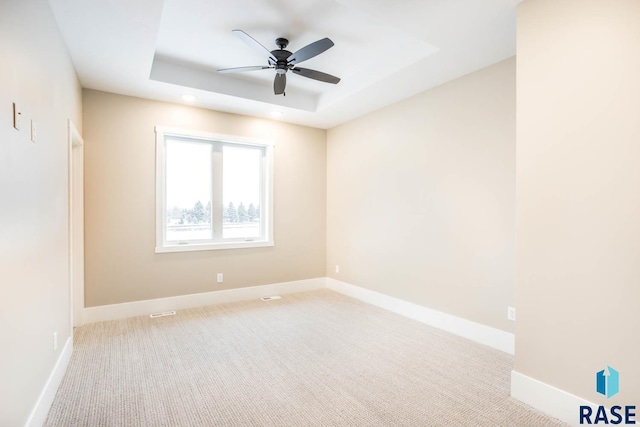 carpeted empty room featuring ceiling fan and a tray ceiling