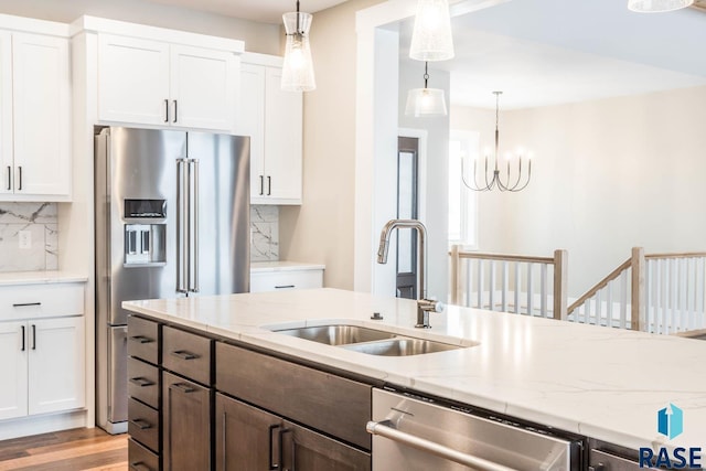 kitchen with white cabinetry, sink, hanging light fixtures, stainless steel appliances, and light stone countertops