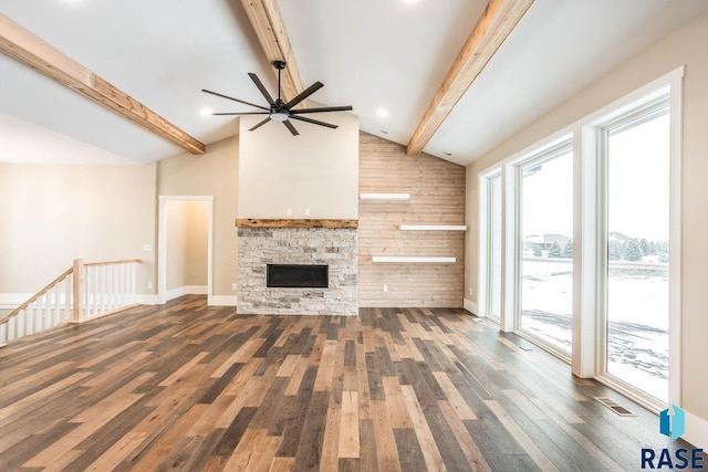 unfurnished living room with dark wood-type flooring, ceiling fan, lofted ceiling with beams, a stone fireplace, and wood walls