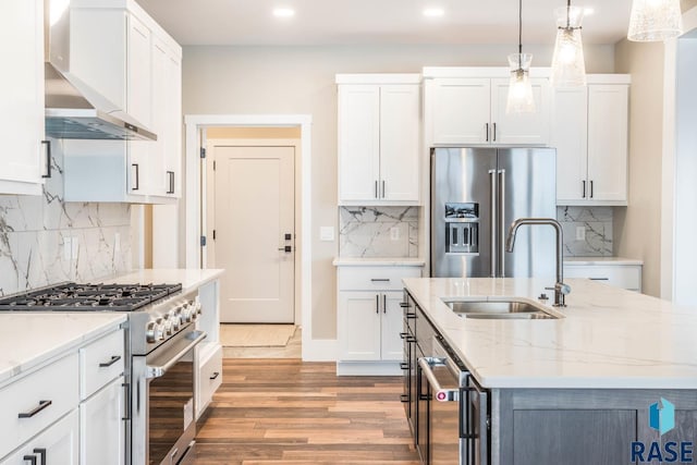 kitchen featuring wall chimney exhaust hood, high quality appliances, decorative light fixtures, and white cabinets