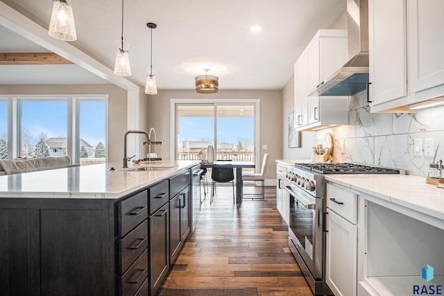 kitchen with sink, high end stainless steel range oven, white cabinets, decorative light fixtures, and wall chimney exhaust hood