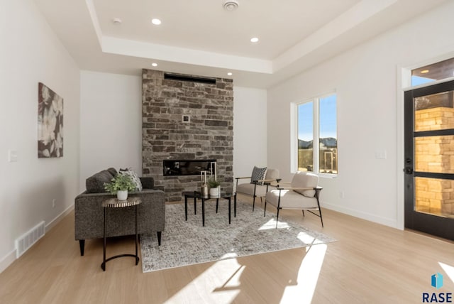 living room with a fireplace, a raised ceiling, and light wood-type flooring