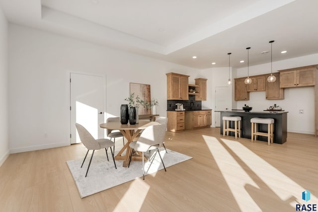 dining space with a raised ceiling and light wood-type flooring