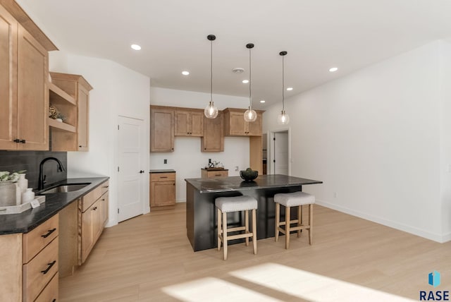 kitchen with light brown cabinetry, sink, a center island, hanging light fixtures, and light hardwood / wood-style floors