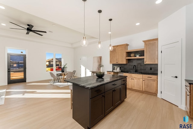 kitchen with sink, dark stone counters, hanging light fixtures, a center island, and light hardwood / wood-style flooring