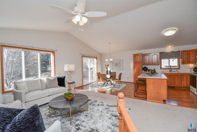 living room with ceiling fan with notable chandelier, lofted ceiling, sink, and light hardwood / wood-style flooring