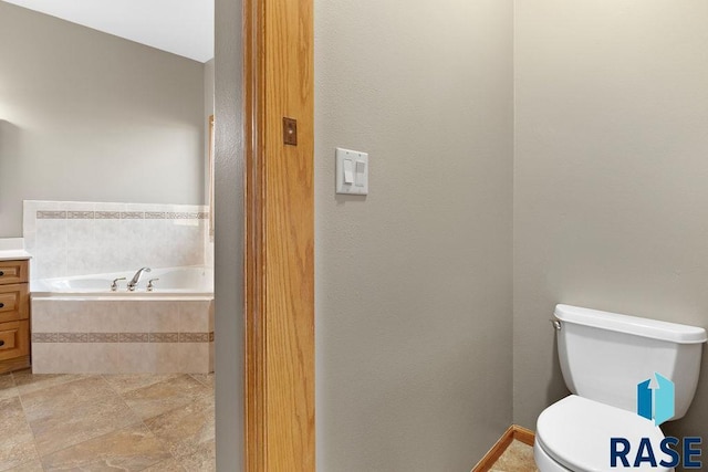 bathroom with a relaxing tiled tub, vanity, and toilet