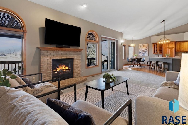 living room featuring lofted ceiling, a fireplace, light hardwood / wood-style flooring, and a notable chandelier