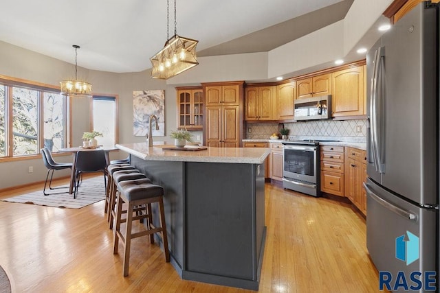 kitchen with pendant lighting, tasteful backsplash, an island with sink, stainless steel appliances, and light hardwood / wood-style flooring