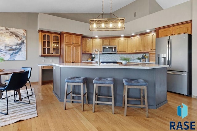 kitchen featuring backsplash, stainless steel appliances, light hardwood / wood-style floors, an island with sink, and a kitchen bar