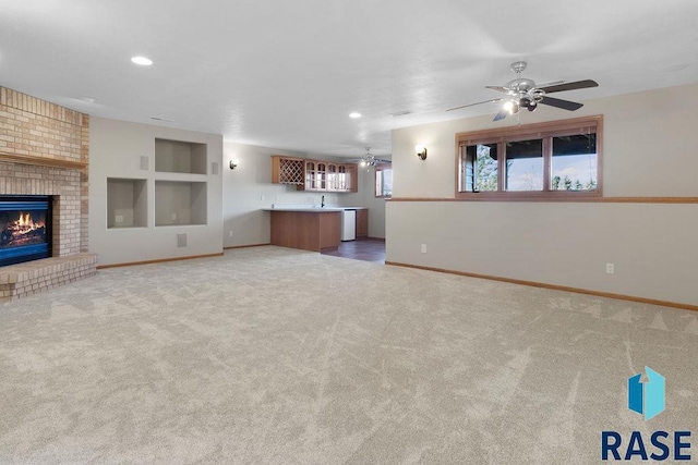 unfurnished living room with a brick fireplace, carpet floors, indoor wet bar, and ceiling fan