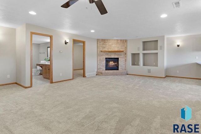 unfurnished living room featuring a brick fireplace, built in shelves, light colored carpet, and ceiling fan